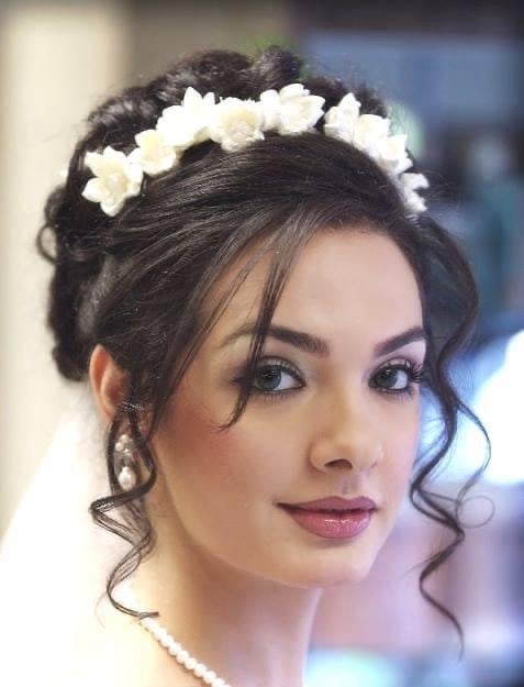 Woman with dark upswept hair wearing white flower crown and pearl necklace, elegant bridal styling