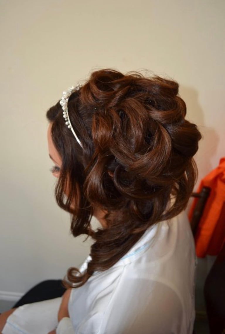 Back view of woman with long brown curled hair styled with a pearl headband, wearing white top