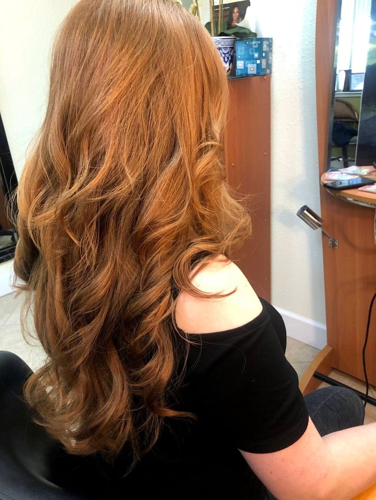 Person with long, wavy copper-brown hair wearing a black off-shoulder top, shown from behind