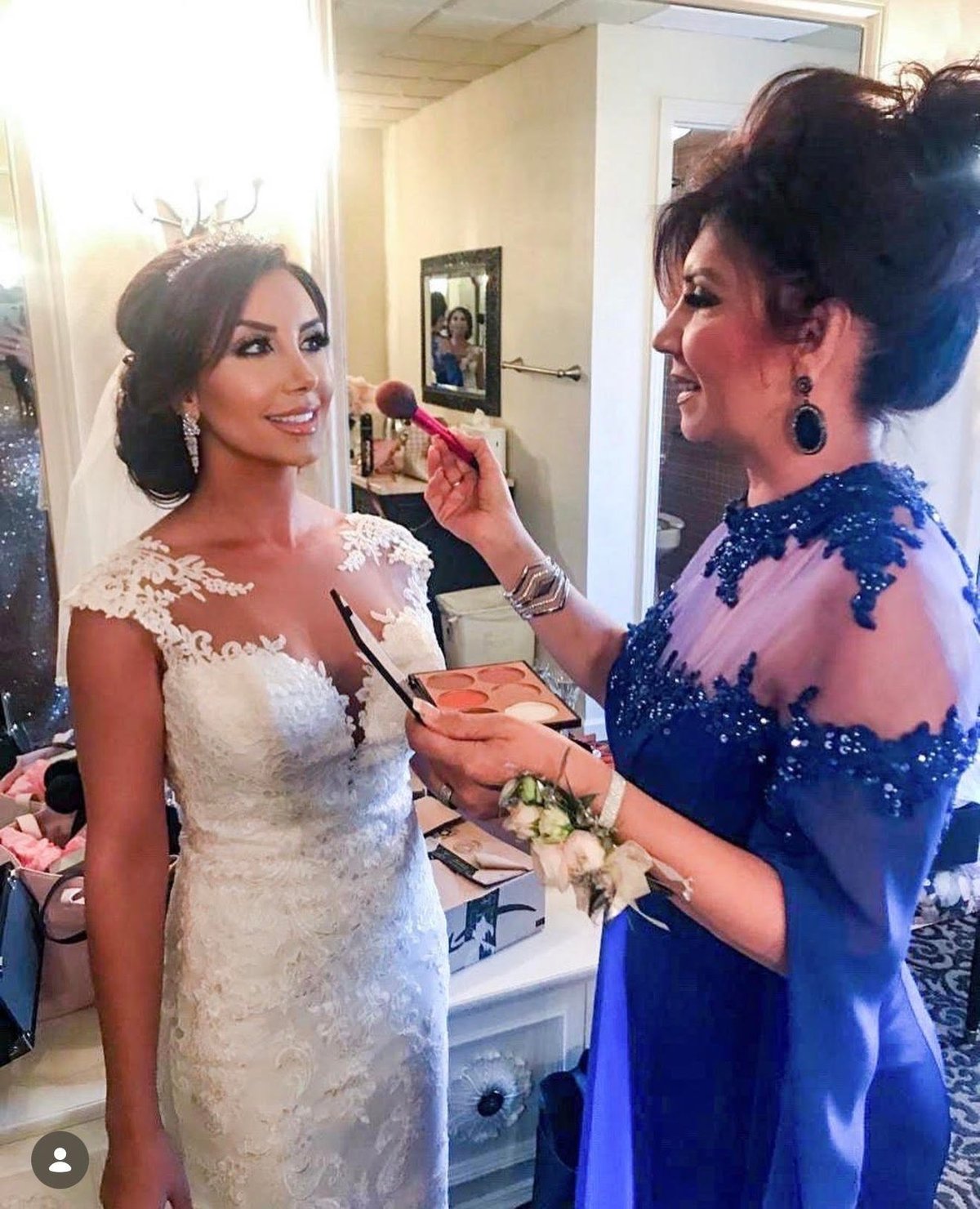 Makeup artist applies cosmetics to bride in white lace dress before wedding ceremony